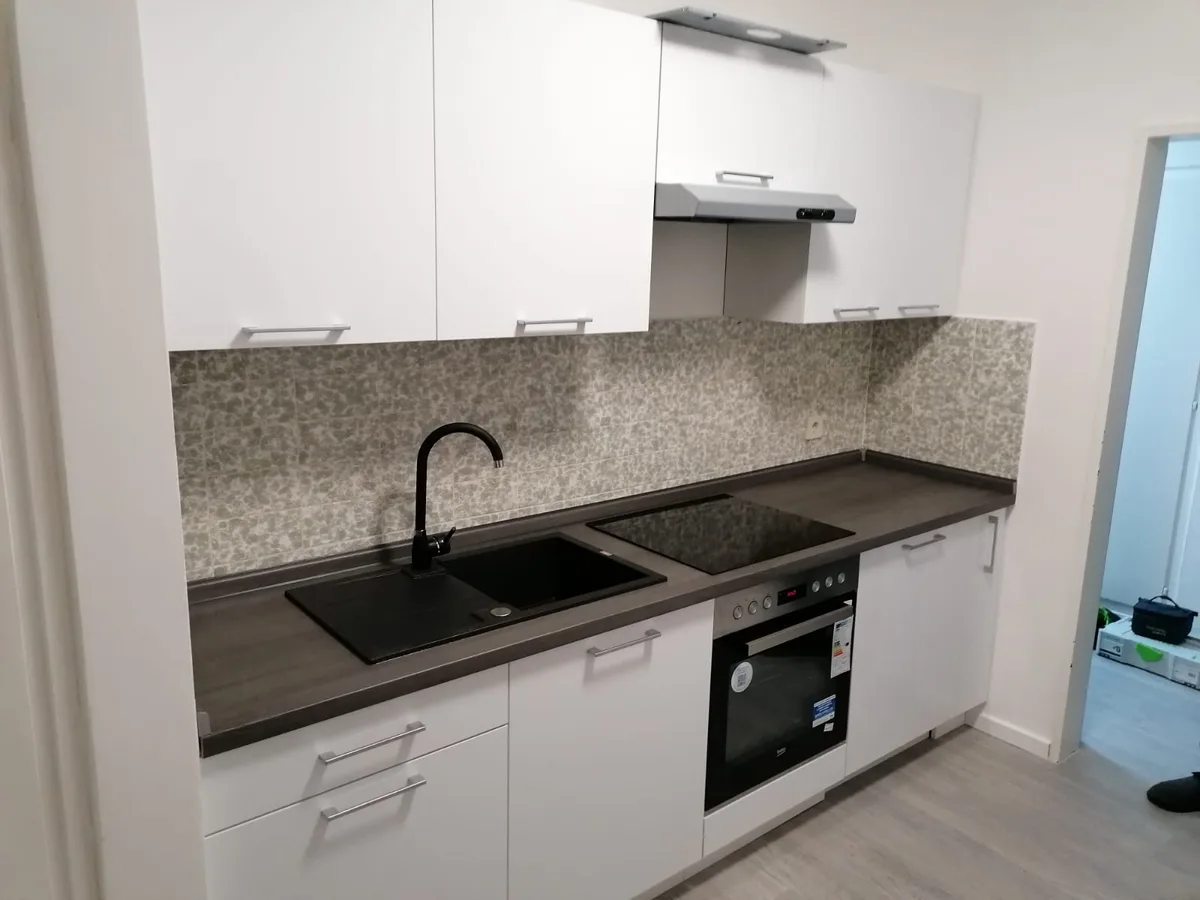 Weiße Küche mit Granitoptik-Arbeitsplatte, schwarzer Spüle und Backofen