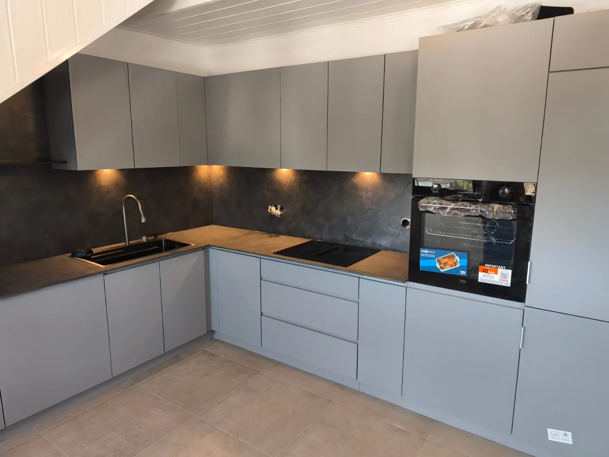 Graue Küche mit Holzarbeitsplatte, dunkler Rückwand und eingebautem Backofen