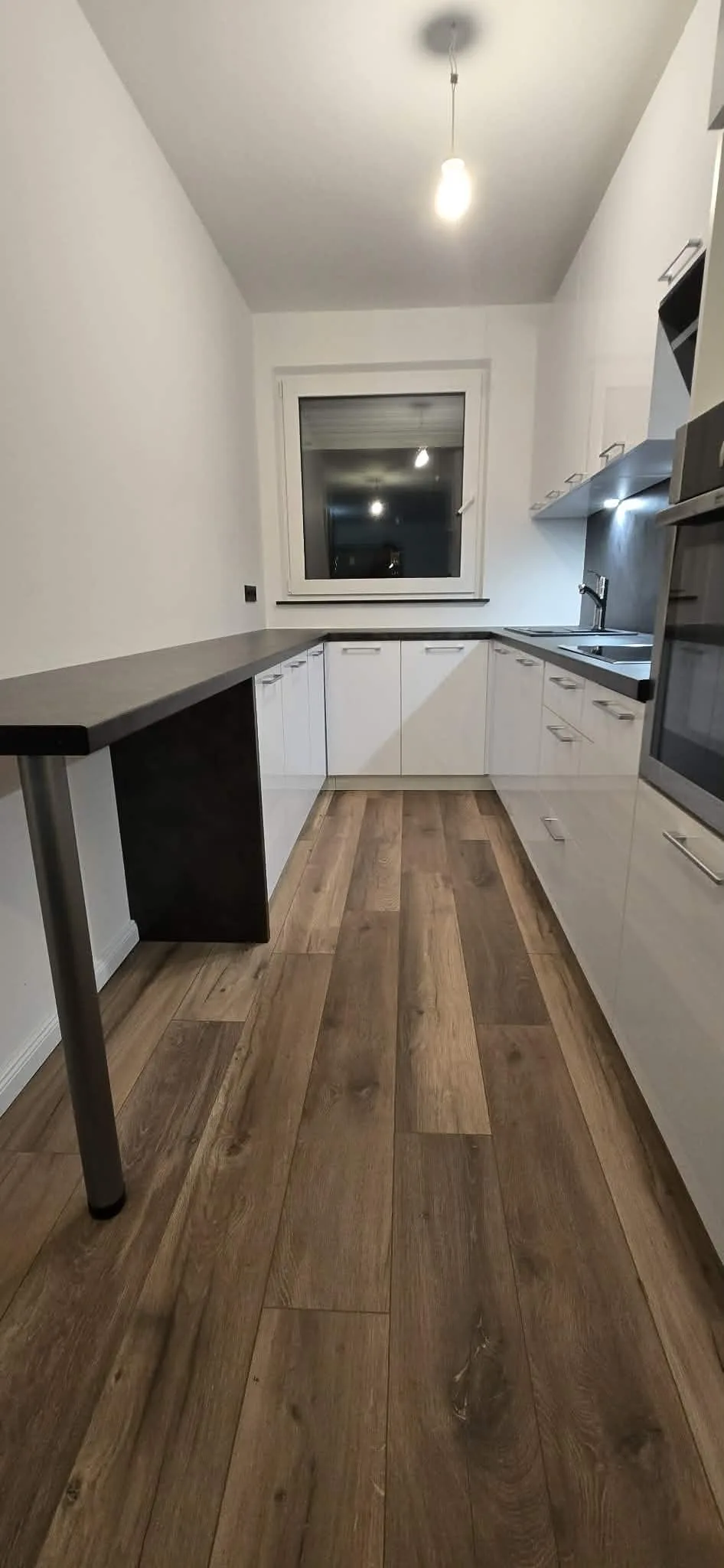 Weiße Küche mit dunkler Theke, Holzfußboden und eingebautem Backofen