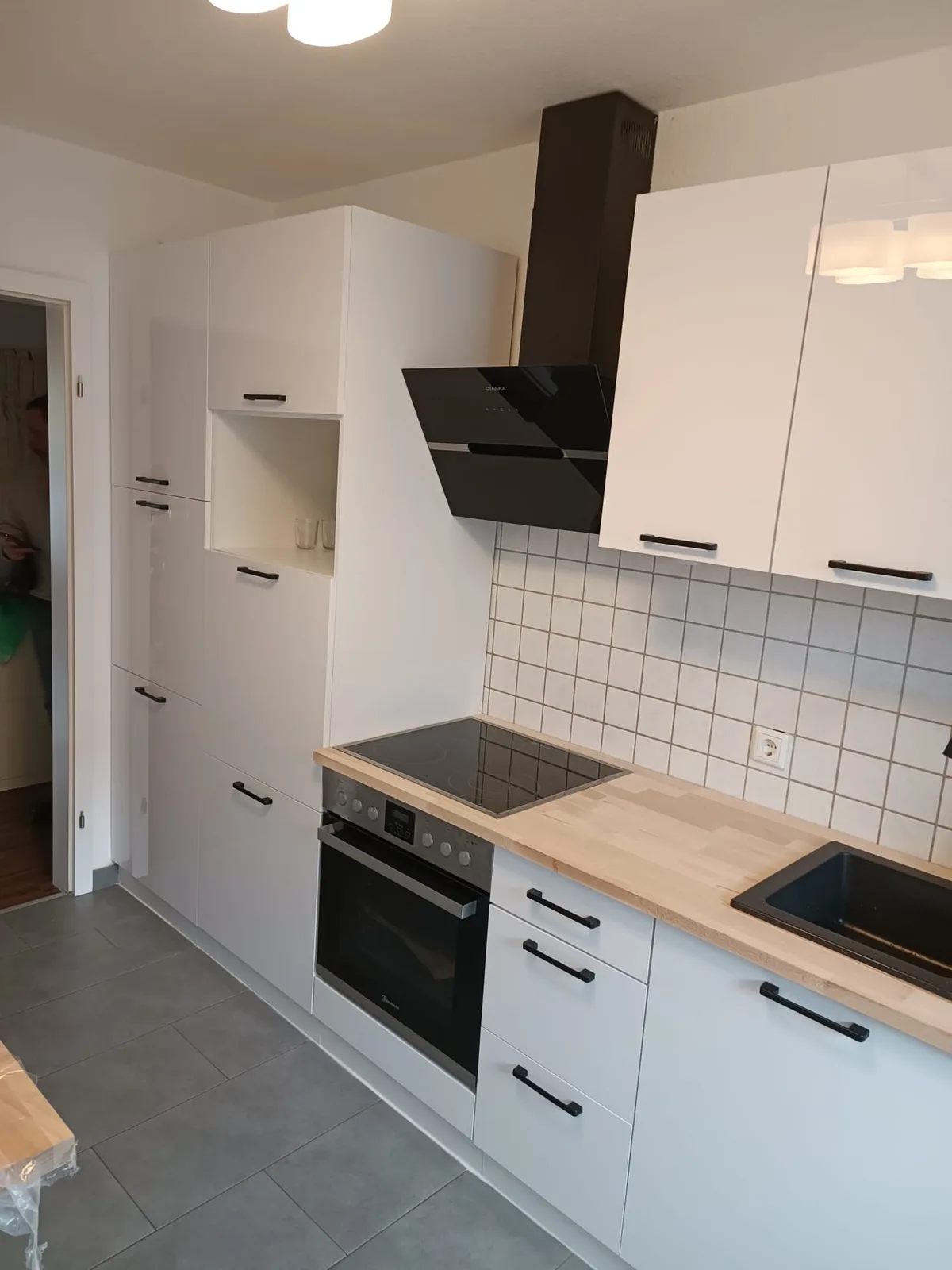 Kleine weiße Küche mit Holzarbeitsplatte, weißen Fliesen und Hochschrank