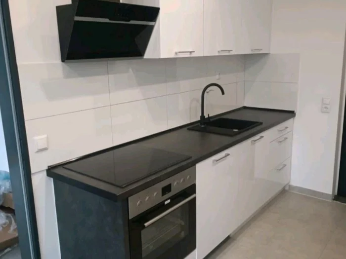 Koyu tezgahlı, siyah evyeli ve davlumbazlı kompakt beyaz mutfak