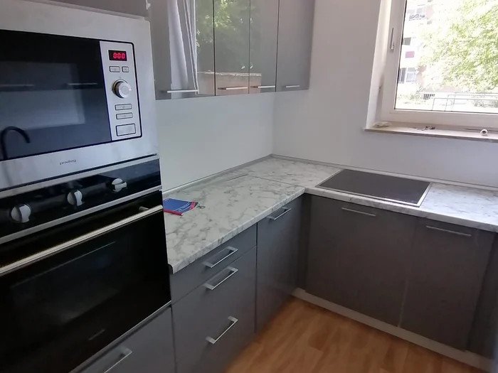 Açık taş görünümlü tezgahlı, pencereli ve yüksek ankastre dolaplı gri mutfak