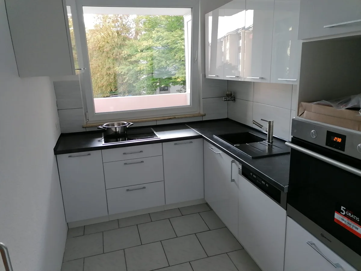 Helle Küche mit dunkler Arbeitsplatte, schwarzer Spüle und Eckfenster